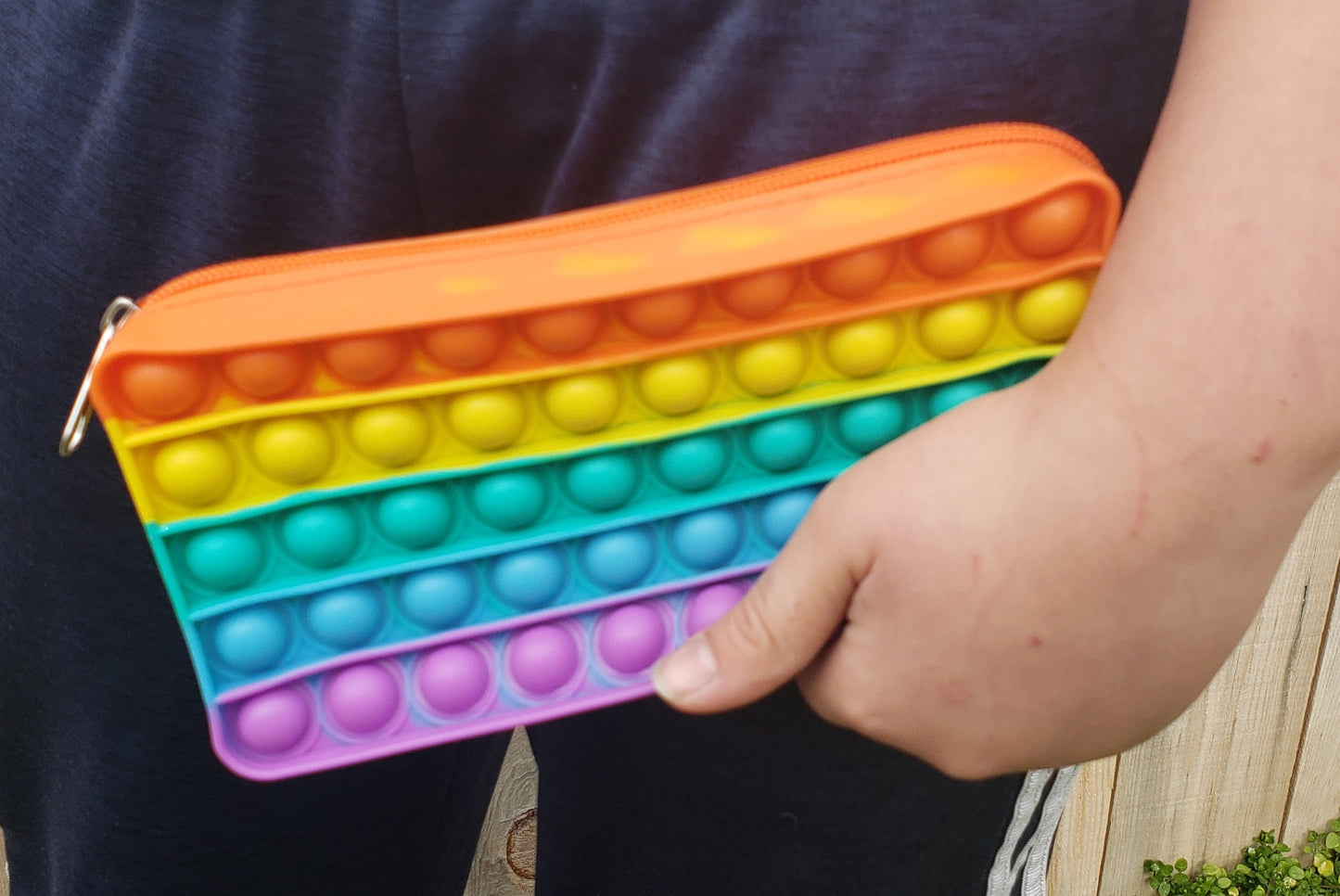 close-up of child holding rainbow pencil pouch clutched in hand