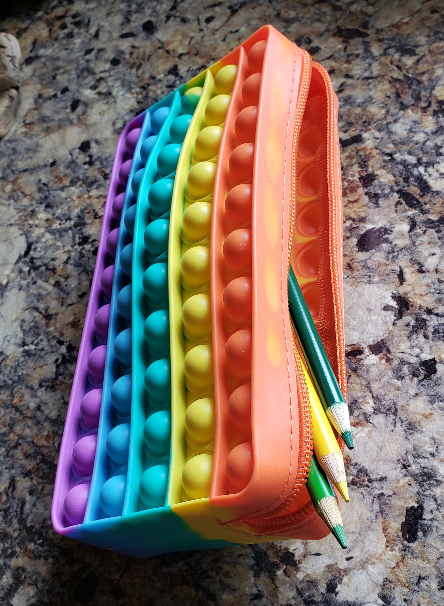 Close-up of silicone rainbow pencil case open with colored pencils sticking out.